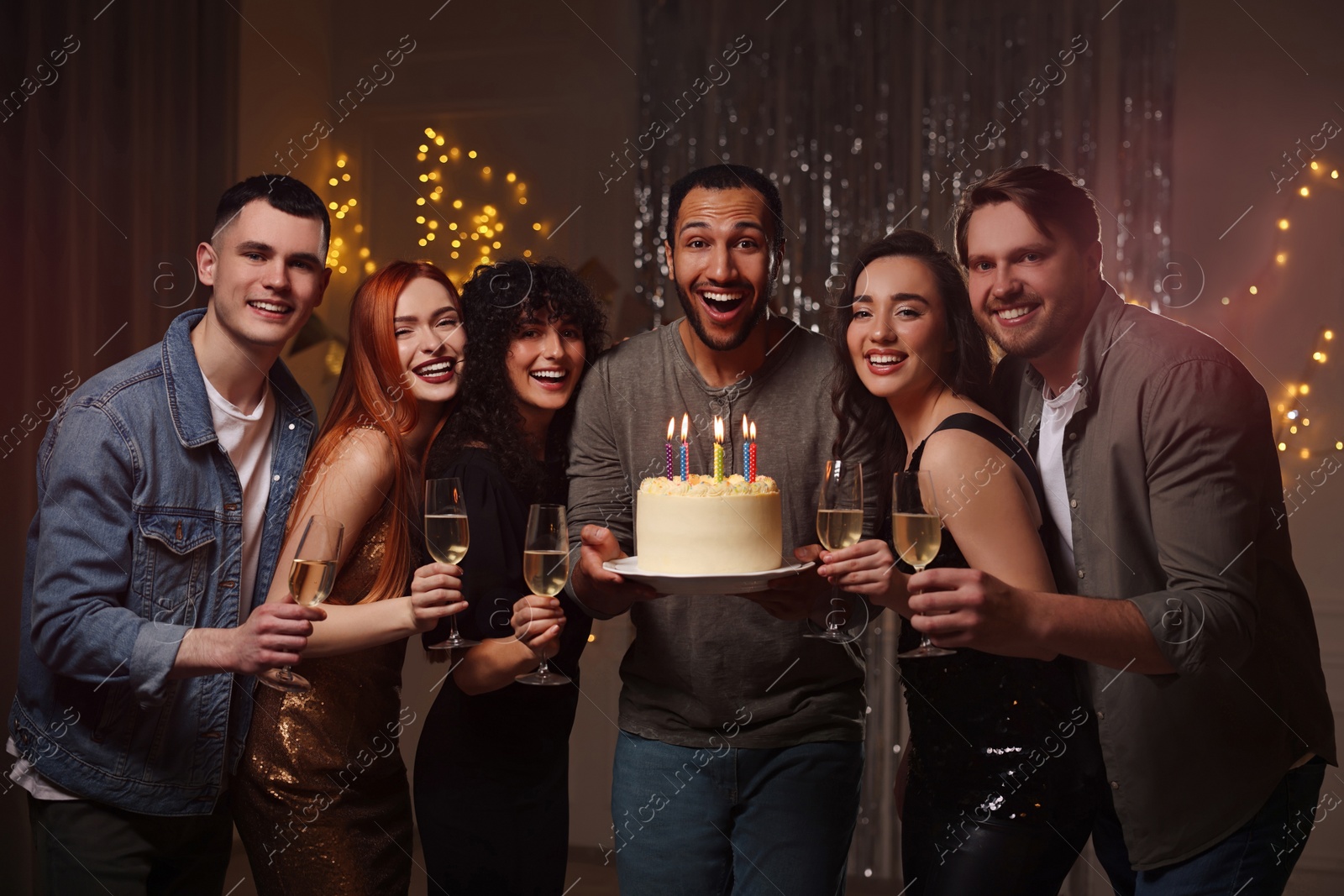 Photo of Happy friends with tasty cake and glasses of sparkling wine celebrating birthday indoors