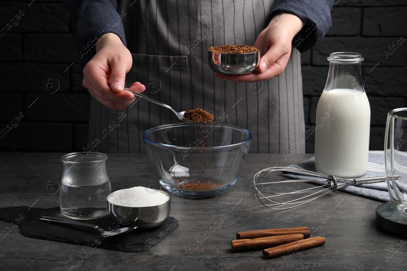 Photo of Making dalgona coffee. Woman pouring instant granules into bowl at grey table, closeup