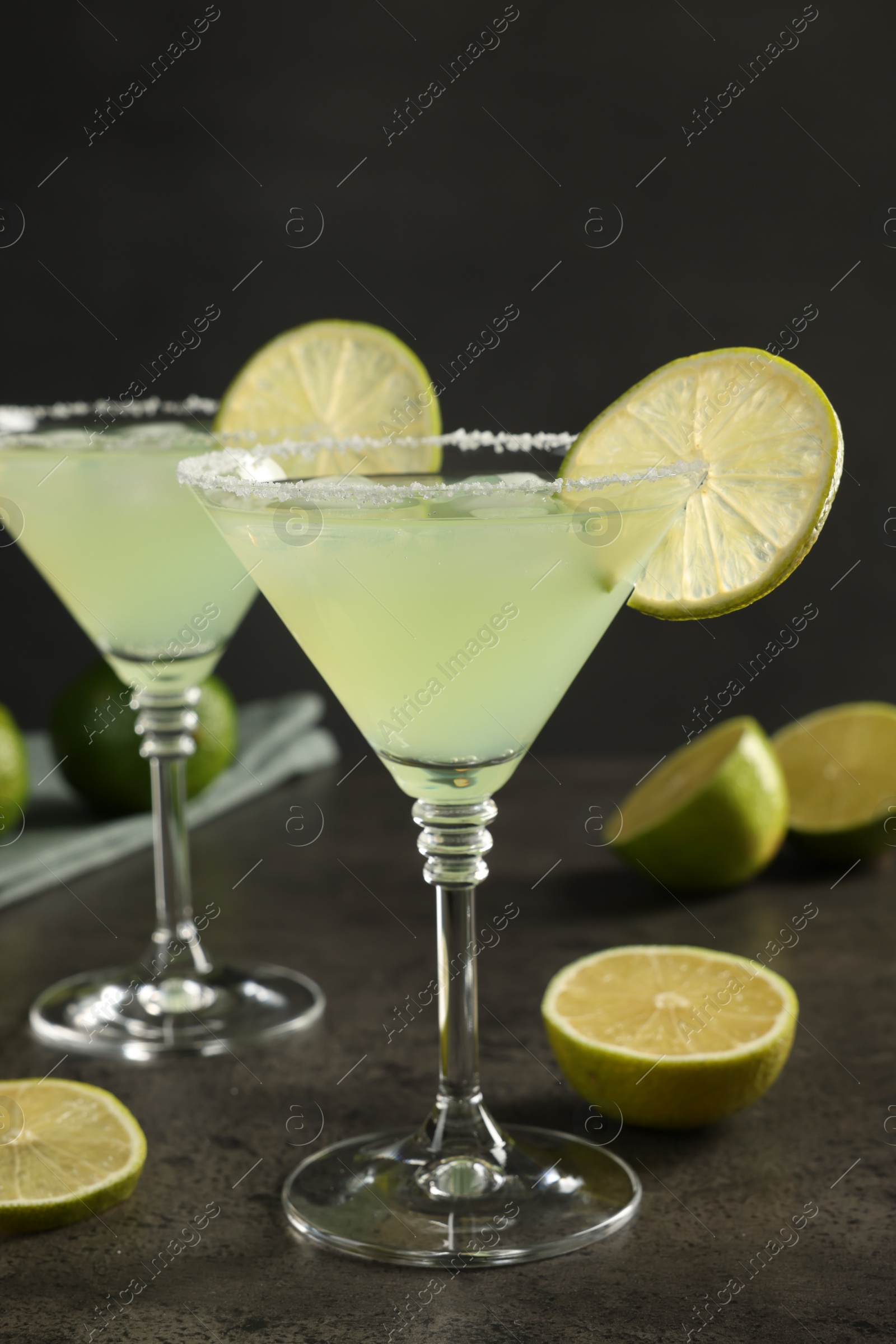 Photo of Delicious Margarita cocktail in glasses and limes on grey table