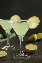 Delicious Margarita cocktail in glasses and limes on grey table