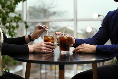 Photo of Couple with glasses of cold cola at table in cafe, closeup