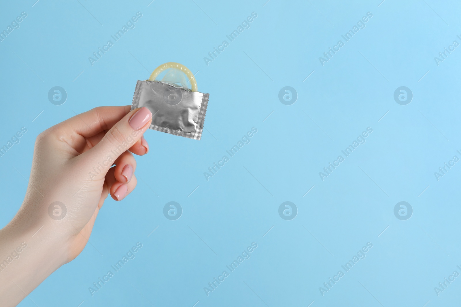 Photo of Woman holding condom on light blue background, closeup. Space for text