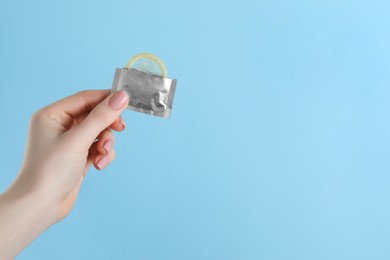 Woman holding condom on light blue background, closeup. Space for text