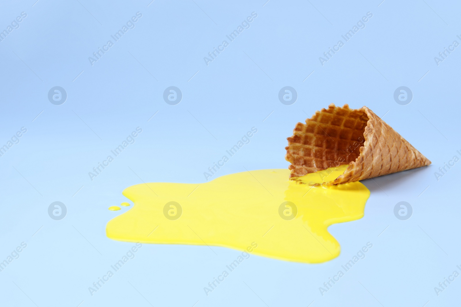 Photo of Melted ice cream and wafer cone on light blue background, space for text