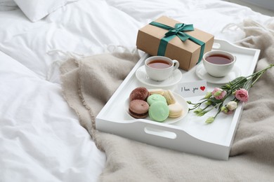 Photo of Tasty breakfast served in bed. Delicious macarons, tea, gift box, flowers and I Love You card on tray