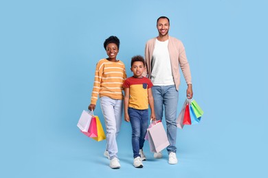 Family shopping. Happy parents and son with colorful bags on light blue background