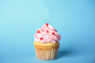 Tasty cupcake with heart shaped sprinkles for Valentine's Day on light blue background