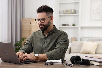 Photo of E-learning. Young man using laptop during online lesson at wooden table indoors