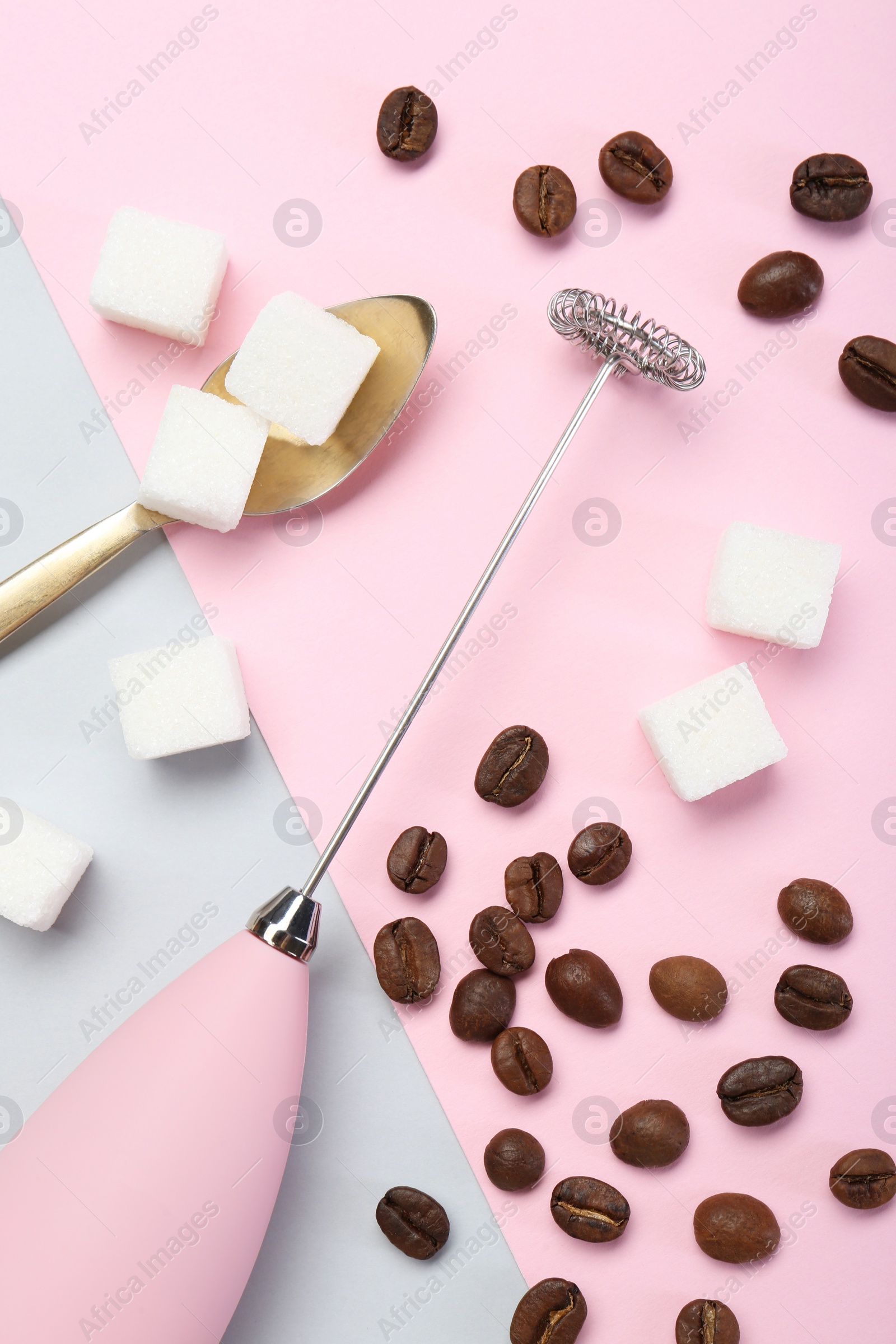 Photo of Pink milk frother wand, coffee beans and sugar cubes on color background, flat lay