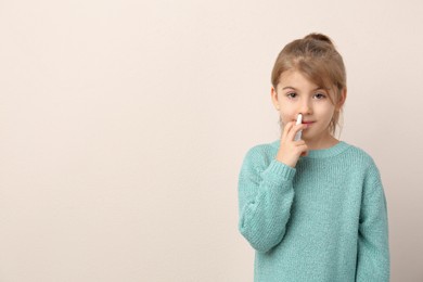 Photo of Sick little girl using nasal spray on beige background. Space for text