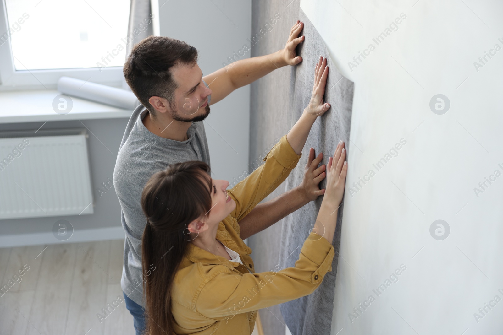 Photo of Couple hanging stylish gray wallpaper in room