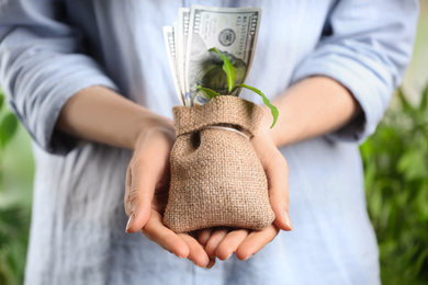Woman holding sack with dollars and green sprout, closeup. Money savings