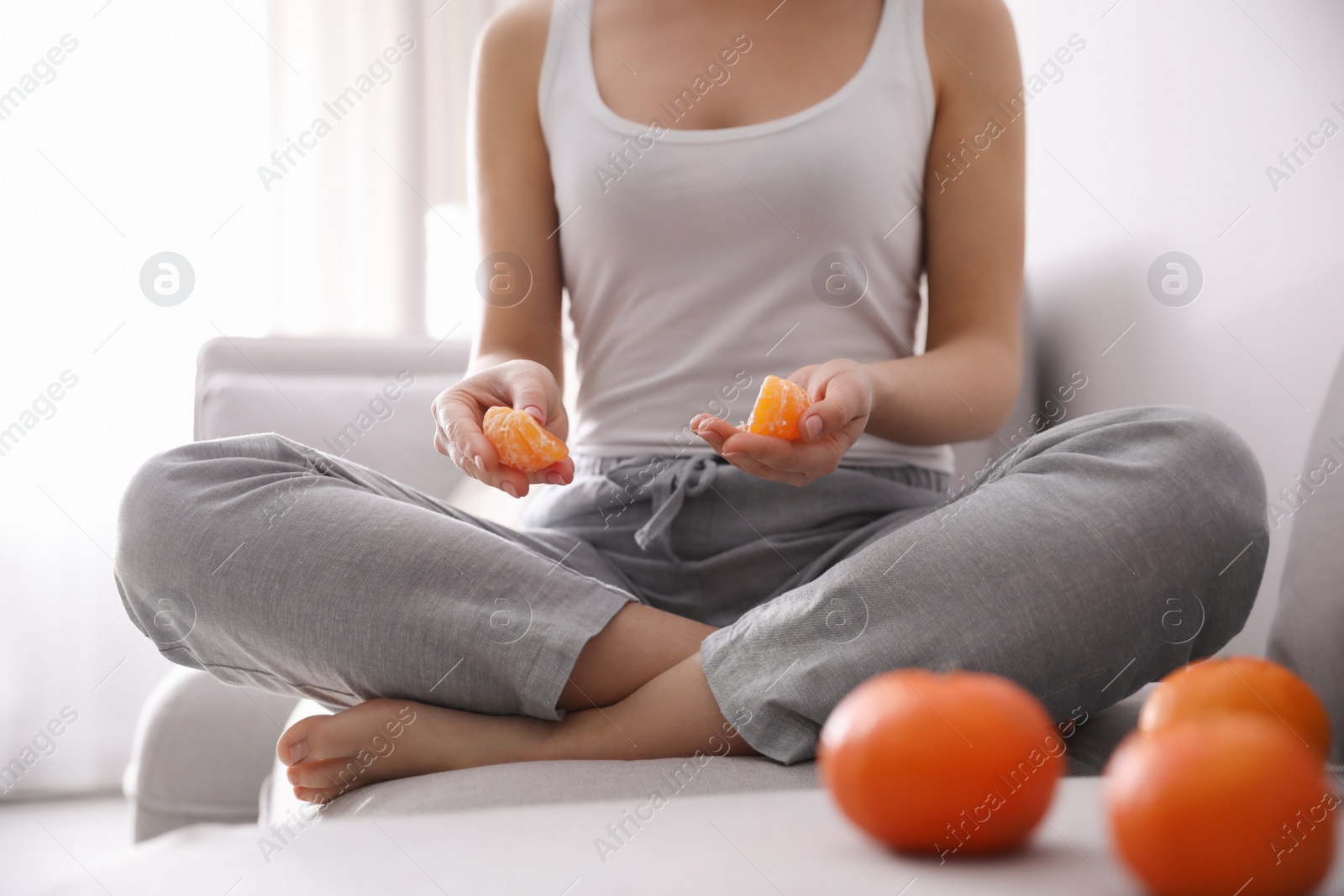 Photo of Young woman with peeled ripe tangerine on sofa indoors, closeup