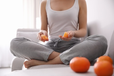 Young woman with peeled ripe tangerine on sofa indoors, closeup
