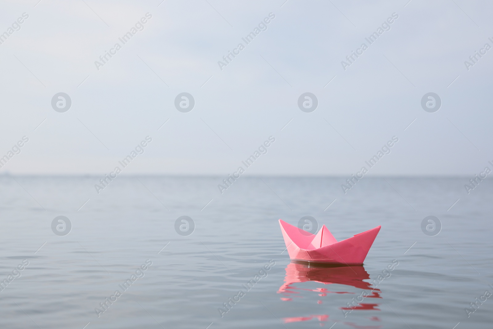 Photo of Pink paper boat on water surface, space for text