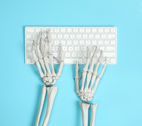 Photo of Human skeleton using computer keyboard on light blue background, top view