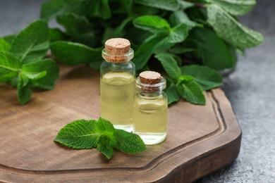 Photo of Bottles of essential oil and mint on grey table, closeup