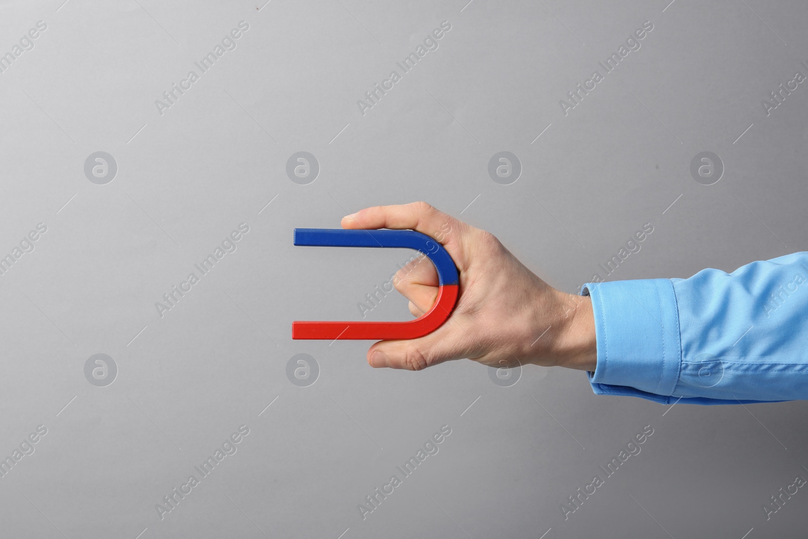 Photo of Man holding magnet on grey background, closeup. Space for text