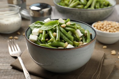 Photo of Delicious salad with green beans, pine nuts and cheese served on wooden table