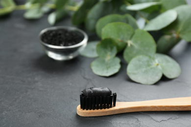 Photo of Bamboo toothbrush with charcoal paste on black stone table, closeup. Space for text