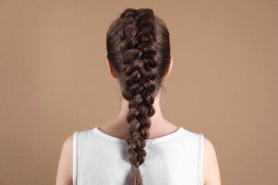 Woman with braided hair on light brown background, back view