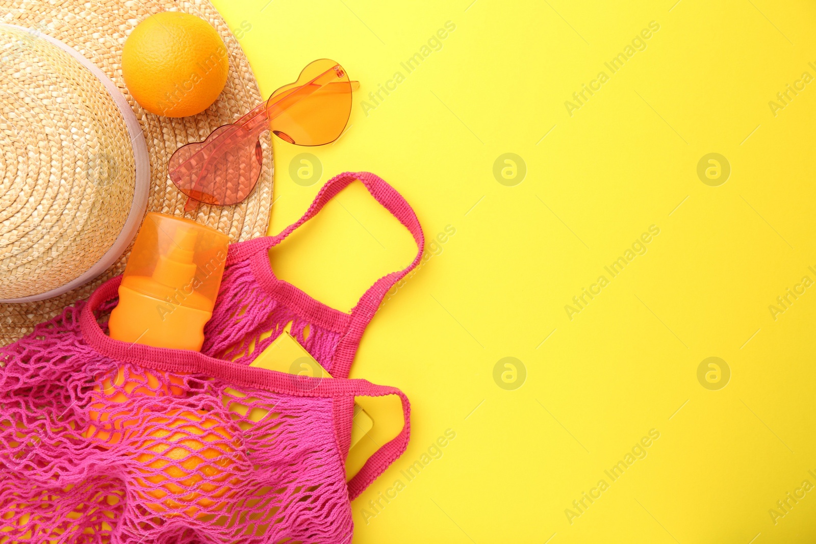Photo of String bag with beach accessories and oranges on yellow background, flat lay. Space for text