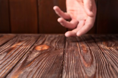 Photo of Man holding hand above wooden table, selective focus. Space for text