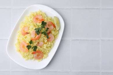 Photo of Delicious risotto with shrimps, lime and parsley on white tiled table, top view. Space for text