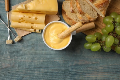 Photo of Flat lay composition with pot of tasty cheese fondue on blue wooden table, space for text