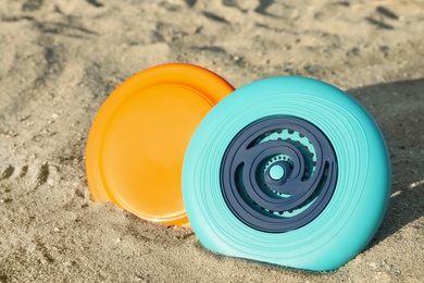 Photo of New plastic frisbee discs on sandy beach, closeup