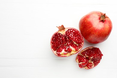 Photo of Fresh pomegranates on white wooden table, top view. Space for text