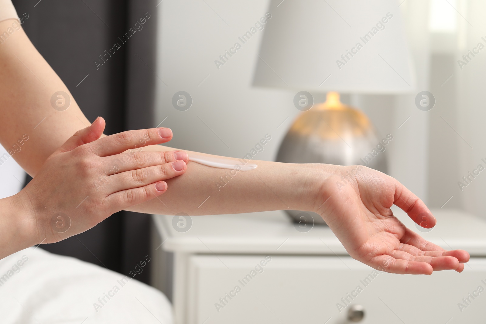 Photo of Young woman with dry skin applying cream onto her arm indoors, closeup