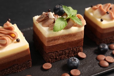 Pieces of triple chocolate mousse cake on black table, closeup