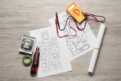 Wiring diagrams and digital multimeter on white wooden table, flat lay