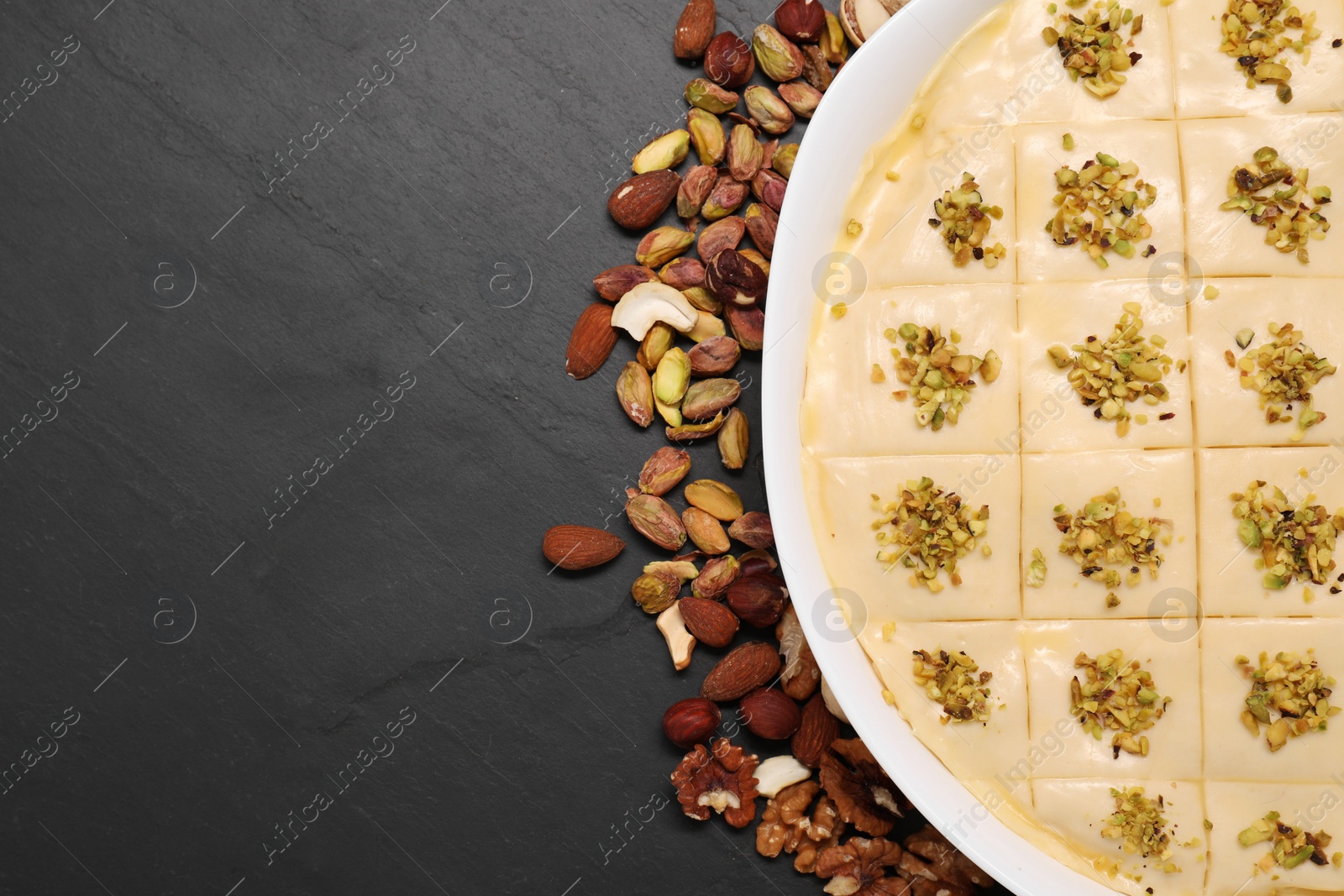 Photo of Making delicious baklava. Raw dough with different nuts on black textured table, flat lay. Space for text
