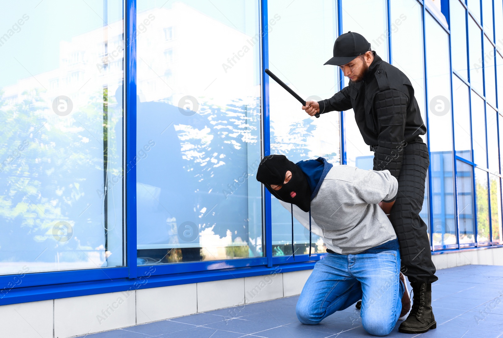 Photo of Police officer with baton arresting masked criminal outdoors