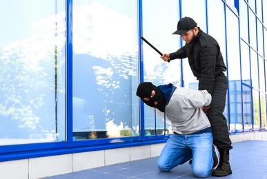 Police officer with baton arresting masked criminal outdoors