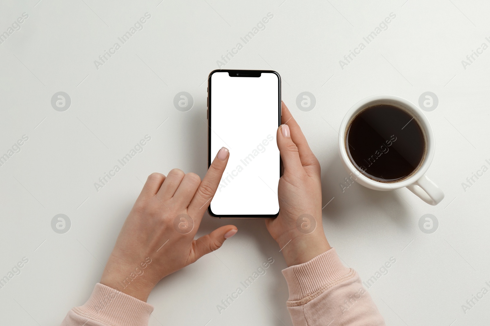 Photo of Woman with smartphone and cup of coffee at white table, top view