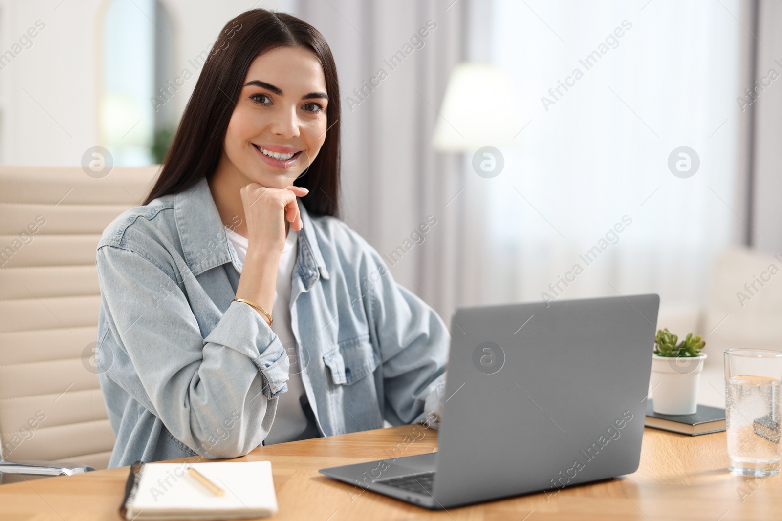 Photo of Young woman watching webinar at table in room