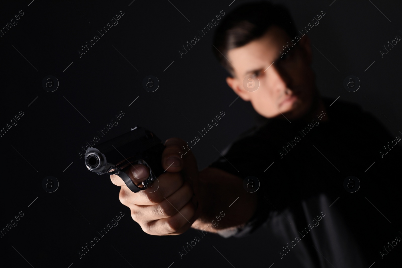 Photo of Professional killer on black background, focus on gun