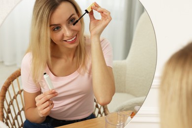 Beautiful woman applying mascara near mirror at home