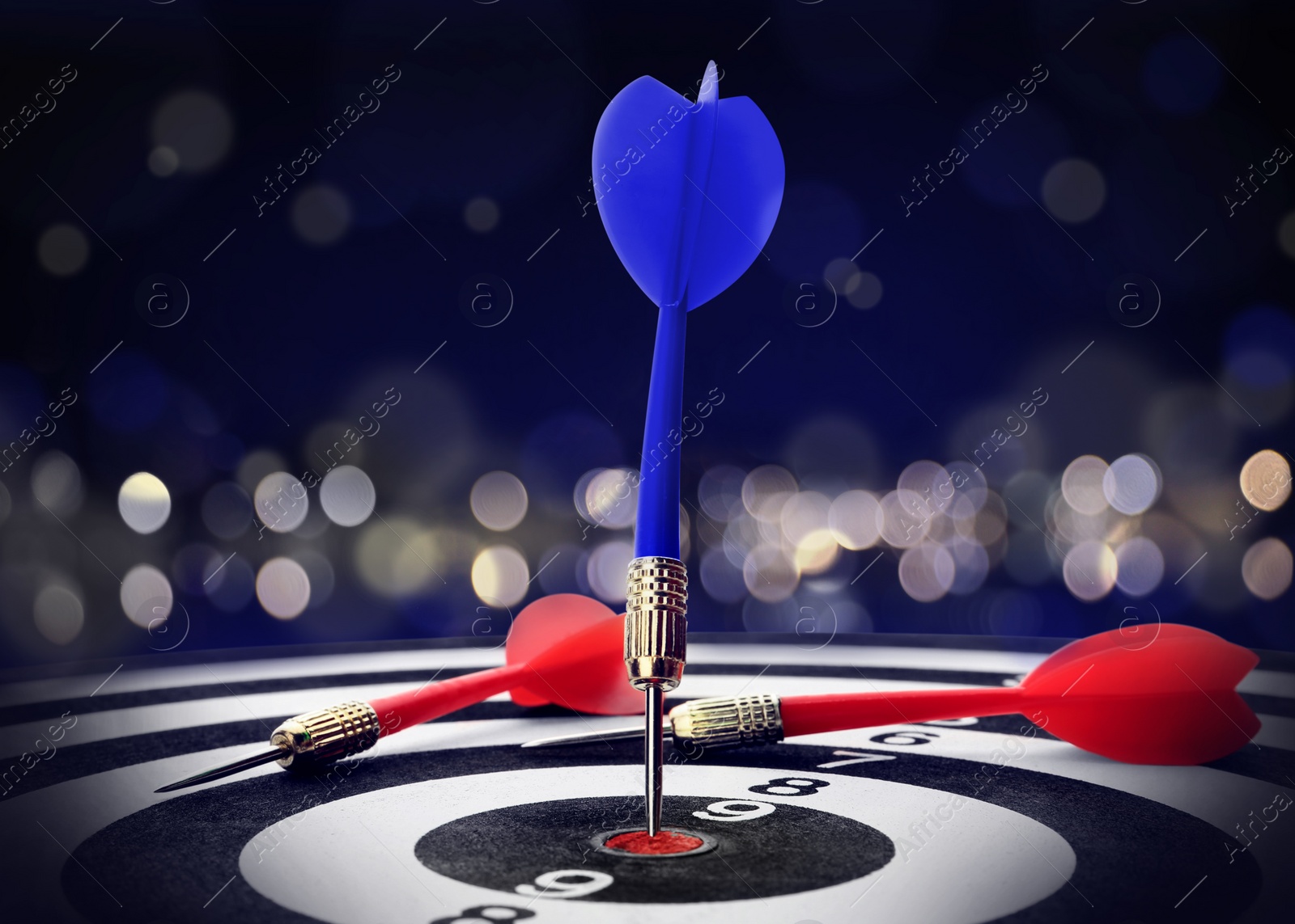 Image of Dart board with blue arrow hitting target against blurred background, bokeh effect