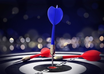 Dart board with blue arrow hitting target against blurred background, bokeh effect