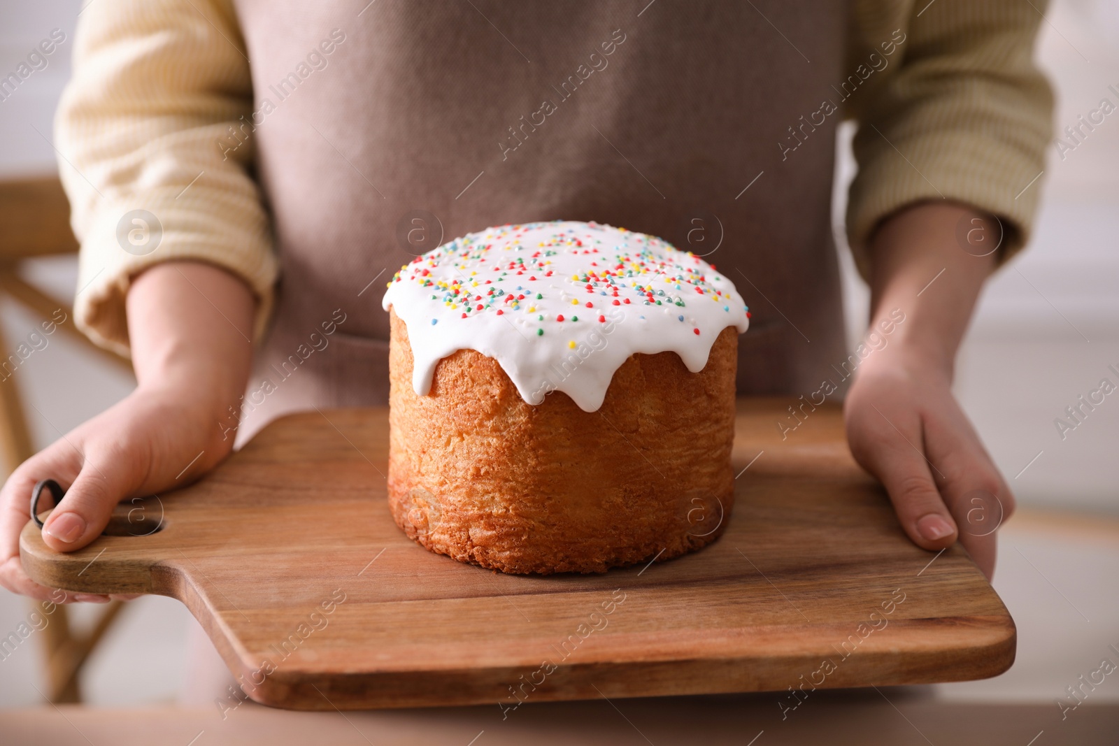 Photo of Young woman holding board with traditional Easter cake in kitchen, closeup