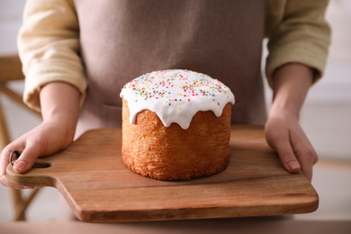 Photo of Young woman holding board with traditional Easter cake in kitchen, closeup