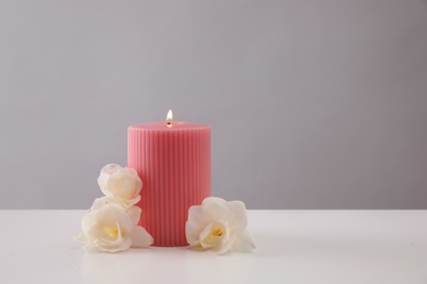 Pink wax candle and flowers on table against grey background. Space for text