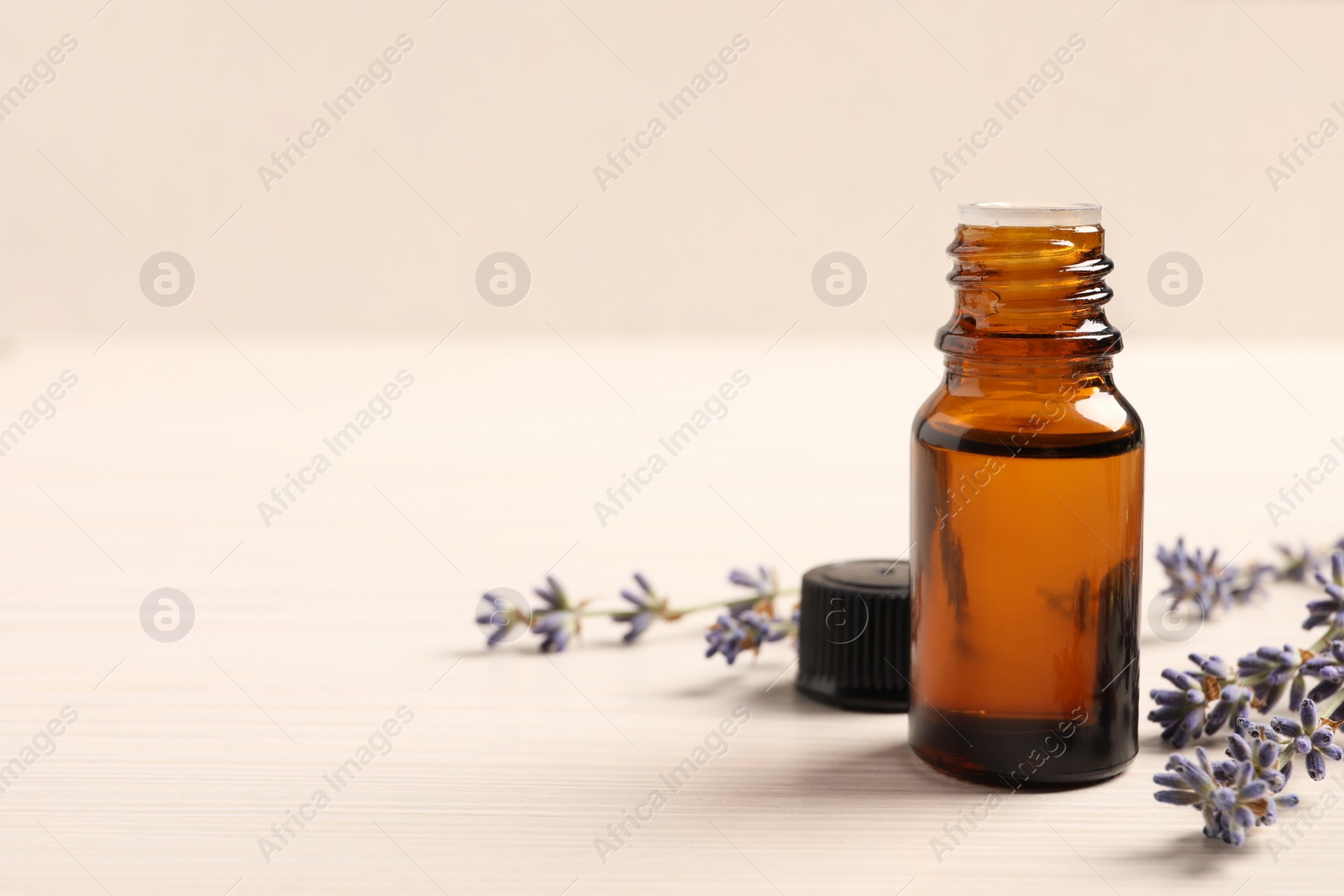 Photo of Bottle of essential oil and lavender flowers on white wooden table, space for text