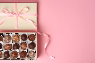Photo of Box of delicious chocolate candies on pink background, top view. Space for text