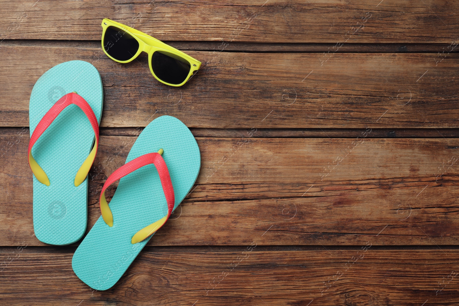 Photo of Stylish flip flops and sunglasses on wooden background, flat lay. Space for text