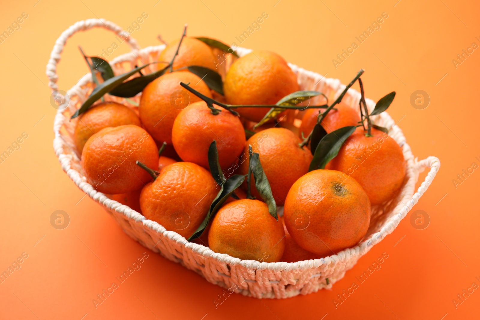 Photo of Fresh ripe tangerines and leaves in basket on orange table